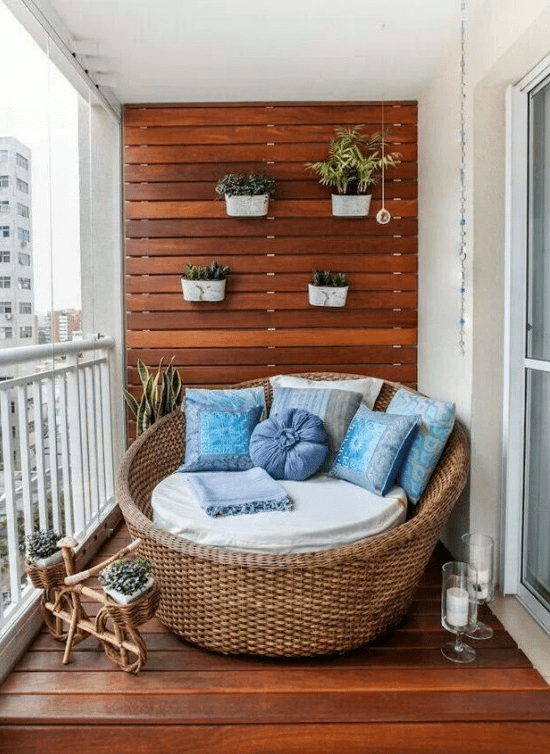 a contemporary balcony clad with stained wood, with a wicker chair, potted greenery and succulents and bright textiles