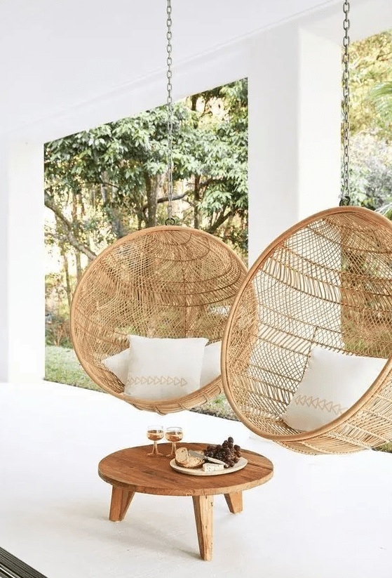 a contemporary porch with two round rattan suspended chairs, with a low coffee table and some pillows is lovely
