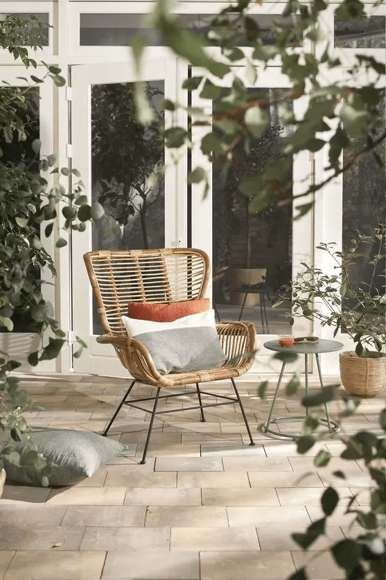 a cool rattan chair styled with soft pillows, with a side table and some greenery around is a lovely piece for outdoors