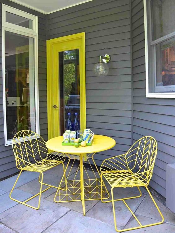 a cool small porch with a bold yellow door, a yellow table, metal chairs is bright and lively