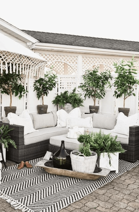 a cozy farmhouse patio with a black wicker sofa and neutral pillows and potted greenery around is a lovely and welcoming space