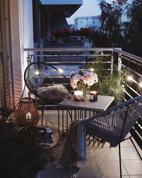a cozy modern balcony with round chairs and a coffee table, lanterns, lights and some greenery is cool