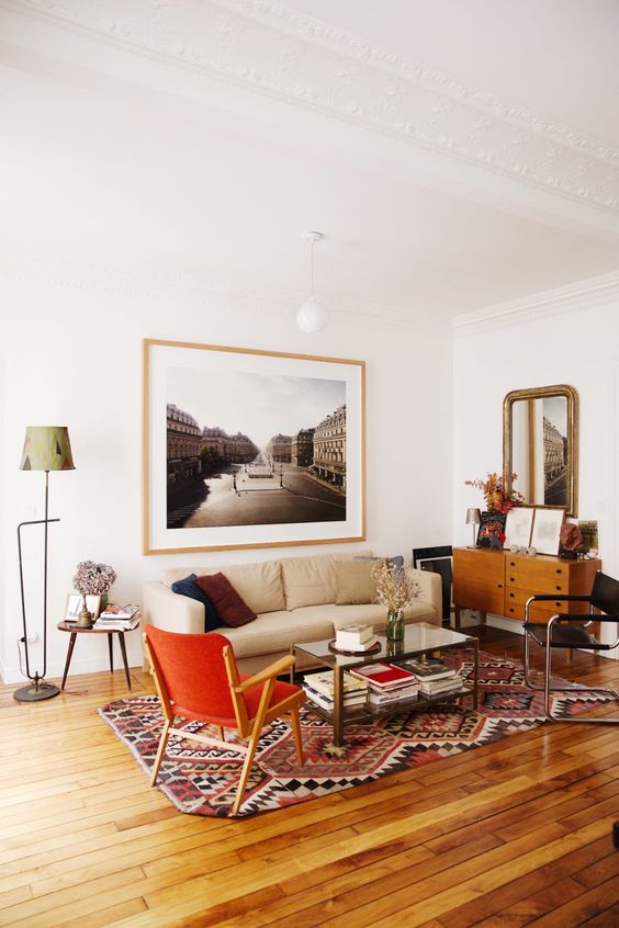 a cozy modern living room with a neutral sofa and black and red chair, a bold boho rug, a sideboard, a mirror and some art