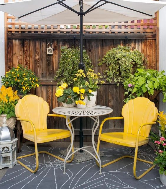 a cozy outdoor nook with an umbrella, a couple of bold yellow chairs, a coffee table and lots of blooms, mostly yellow ones