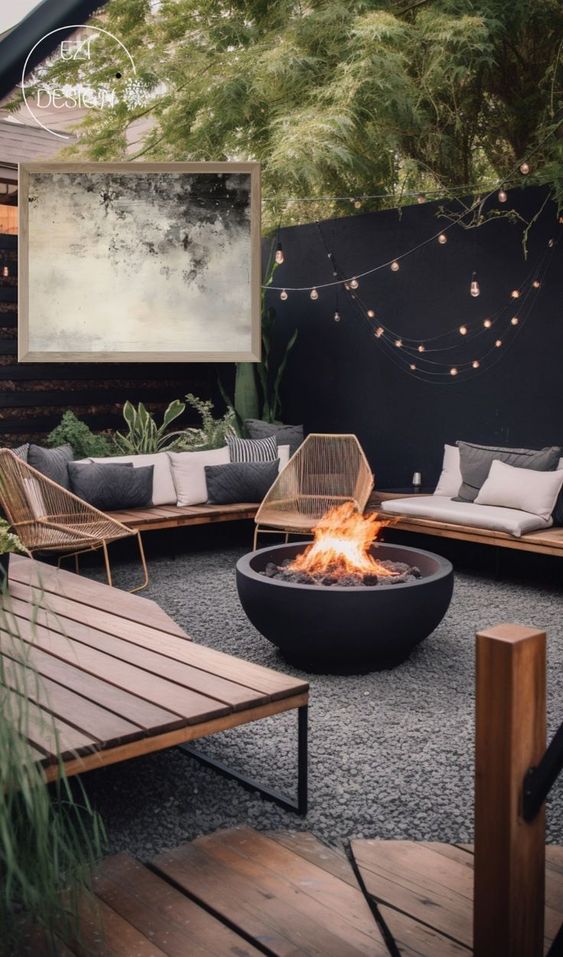 a cozy outdoor space with a black fence, modern stained outdoor furniture, some pillows, a fire pit and some greenery plus lights