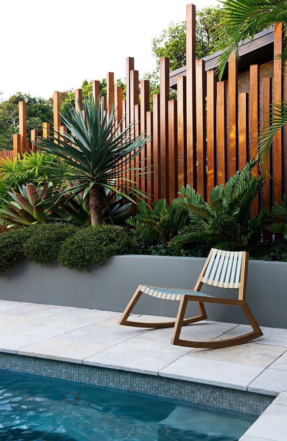 a creative stained fence paired with a tall raised garden bed, with shrubs, greenery and tropical plants are a fantastic idea
