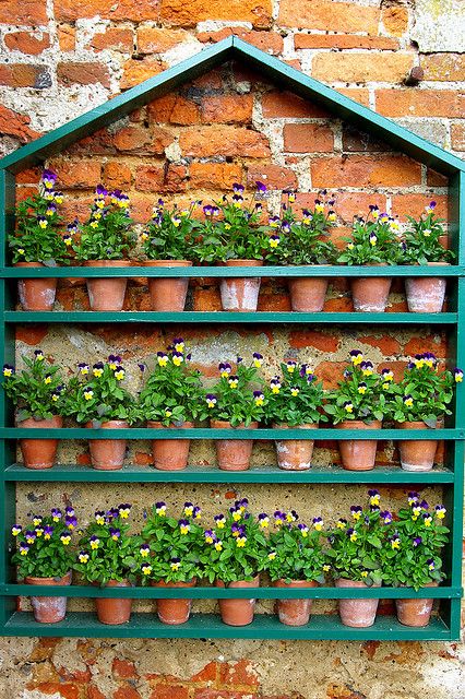 a creative vertical garden of a house-shaped frame with shelves holding various planters with blooms is a super cool and fun decor idea