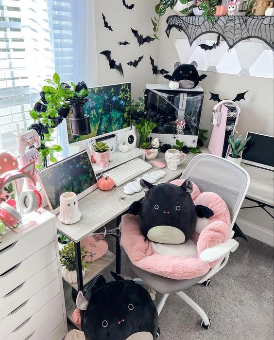 a cute Halloween themed gaming desk setup with lots of bats, plush and paper ones, a desk with a PC and some greenery around
