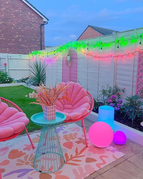 a dopamine decor terrace with neon lights, a couple of pink chairs and pink cushions, a blue side tables and some bright lights