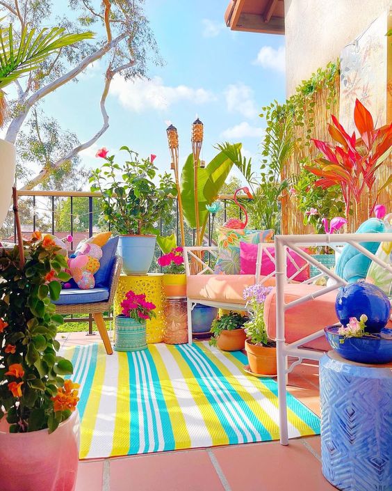 a dopamine terrace with pink and navy chairs, colorful pillows, torpical plants and blooms, a bright rug and some bold pillows
