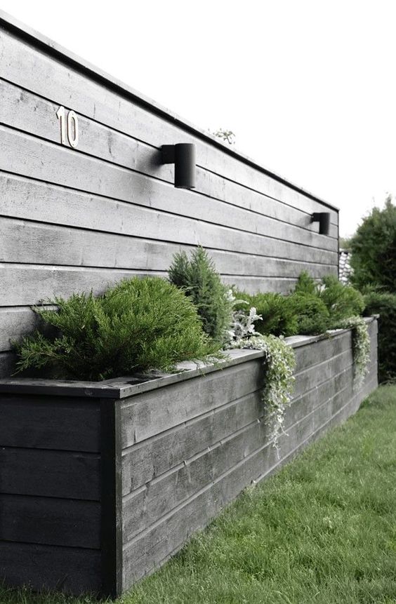 a grey fence plus a raised matching garden bed with greenery and grasses are a lovely combo for a Scandinavian space