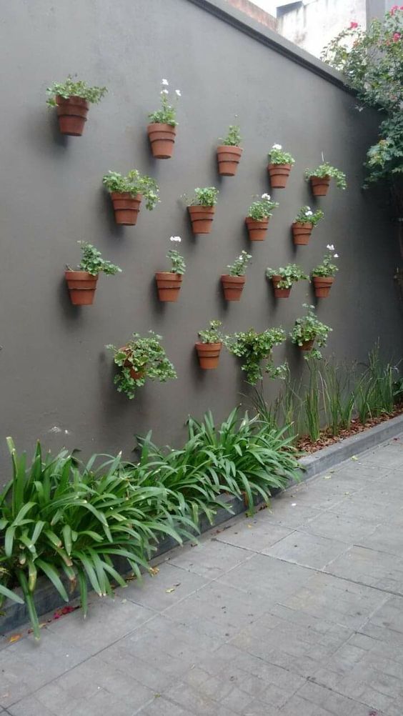 a grey wall with planters with blooms and greenery attached is a cool decoration for a modern garden, it looks nice and chic