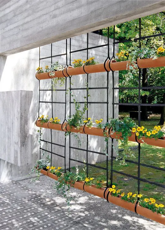 a hanging vertical garden of metal grids and pipe planters attached is a creative alternative to a privacy screen