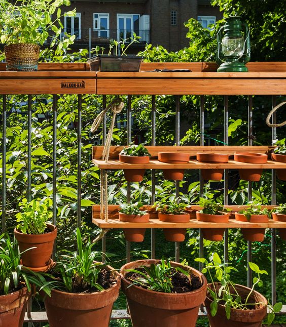 a hanging wooden shelf with some planters with herbs and more planters on the floor are a cool combo for a rustic balcony