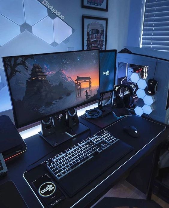a laconic grey gaming setup with sound-proof panels, a black desk and some devices, hex lamps on the PC and artwork