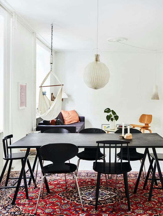 a living and dining room with a bold boho rug, a black table and mismatching chairs, a navy sofa with pillows, a chair and a table