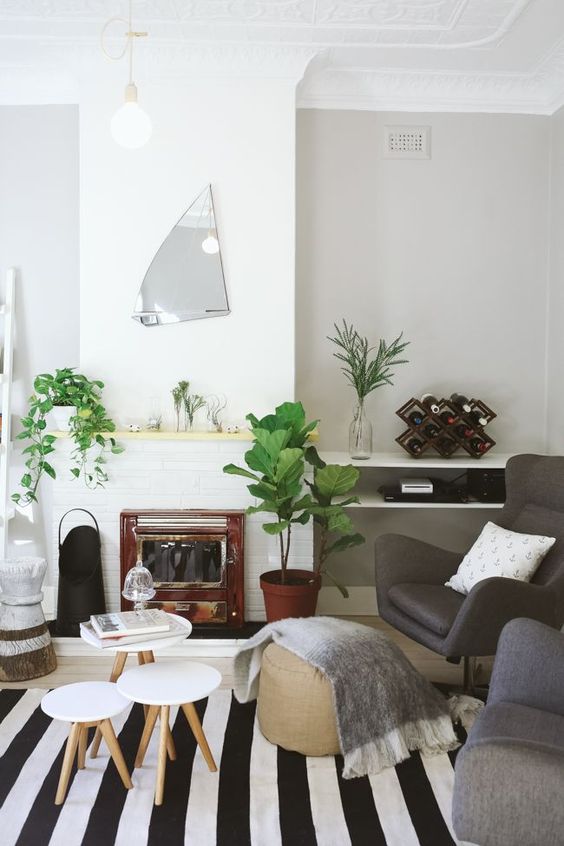 a lovely Scandinavian living room with a built-in fireplace, grey seating furniture, some greenery, side tables and a whimsical mirror