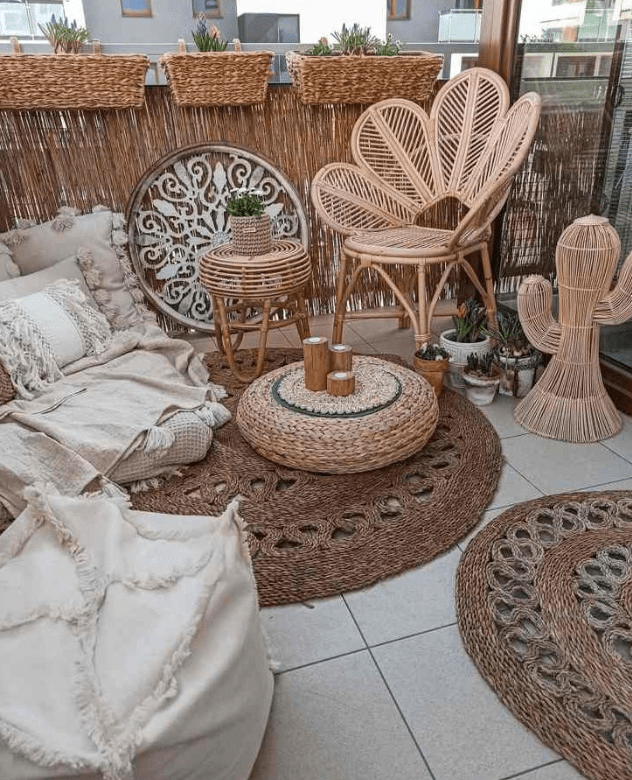 a lovely boho balcony with jute rugs, rattan furniture, a low sofa with lots of pillows, a pouf, a jute pouf with candles and potted plants