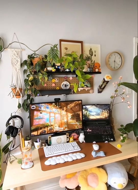 a lovely gaming desk setup with a desk, a shelf with decor and potted plants, some macrame, decor and plush toys is cool