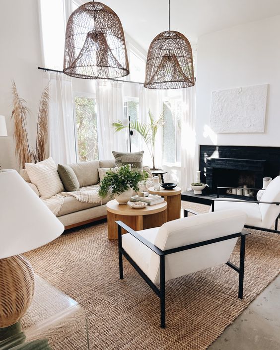 a lovely neutral living room with a fireplace, neutral seating furniture, a jute rug, wooden coffee tables, woven pendant lamps and some decor