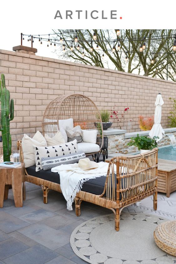 a lovely outdoor boho space with rattan and stained furniture, neutral pillows, plants and blooms and some boho rugs