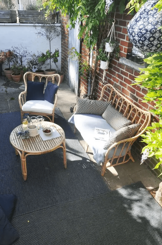 a lovely terrace with a red brick wall, rattan furniture, printed pillows and lots of potted greenery and blooms around