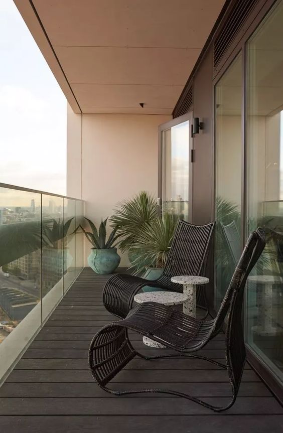 a minimal balcony with black rattan furniture, side tables, potted greenery and a cool view