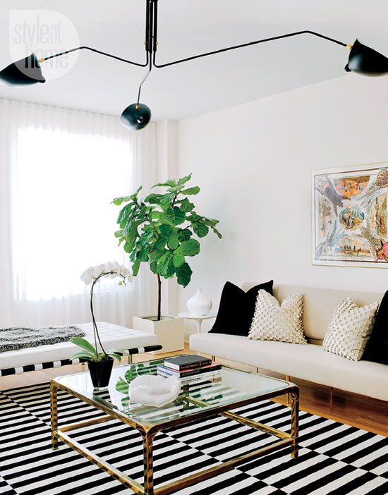 a modern black and white lviing room with a striped rug, a neutral sofa with black and gold pillows, a coffee table, a white daybed and a black chandelier