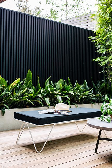 a modern black fence, a raised garden bed with greenery, modern outdoor furniture and some potted greenery