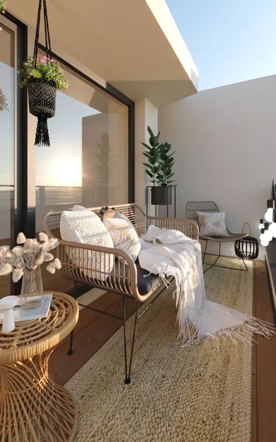 a modern boho balcony with a jute rug, rattan chairs and tables, potted plants and blooms and some lanterns