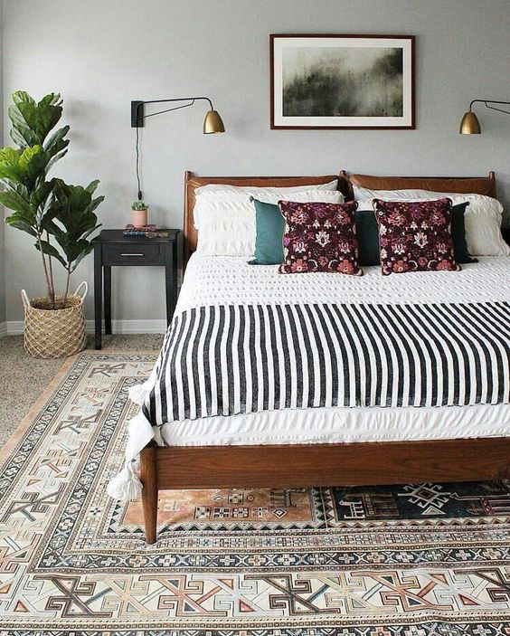 a modern boho bedroom with a printed rug, a bed with printed bedding, a potted plant, black nightstands and lamps