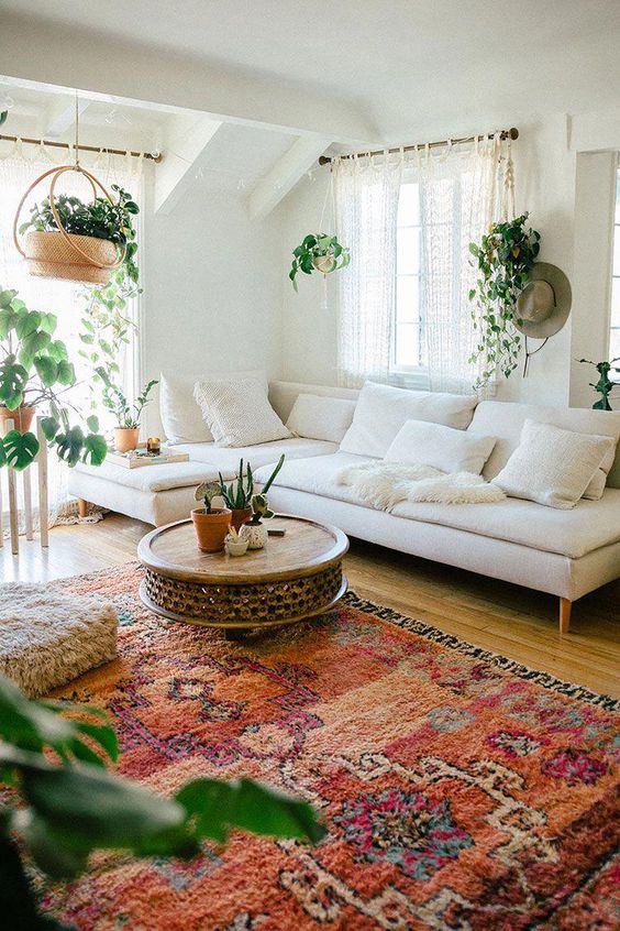 a modern boho living room with a bold boho rug, a white sectional, a coffee table, potted plants and a fluffy cushion