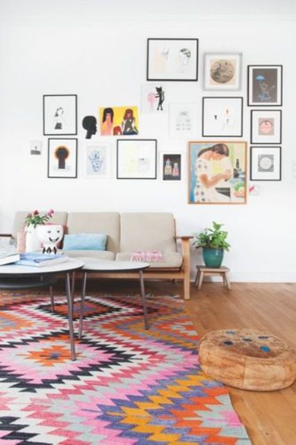 a modern boho living room with a colorful boho rug, a grey sofa, coffee tables, a gallery wall and potted plants