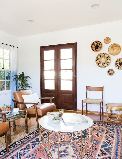 a modern boho space with a bright printed rug, amber leather chairs, coffee tables, a gallery wall of decorative baskets