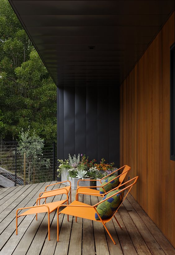 a modern deck styled with orange chairs and footrests, colorful pillows, potted blooms is a cool and fresh space