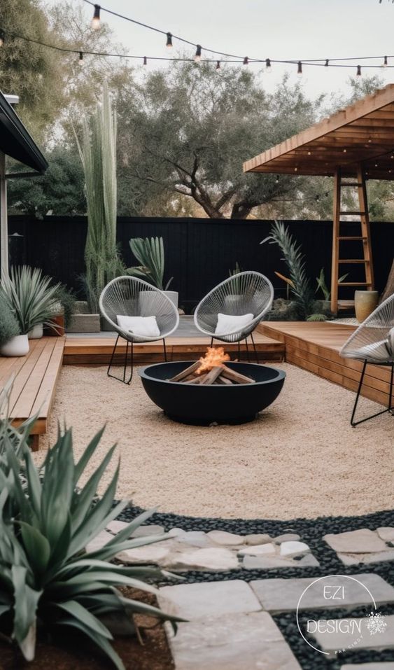 a modern desert backyard with a black fence, a deck, modern furniture, a large fire bowl and some potted plants around