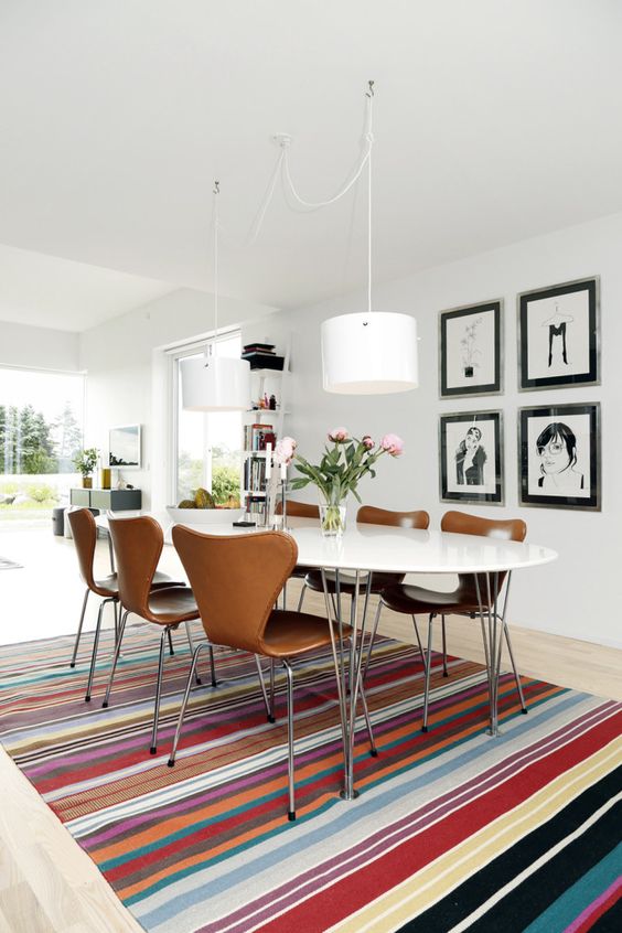 a modern dining room with a colorful rug, an oval table and modern leather chairs, a black and white gallery wall