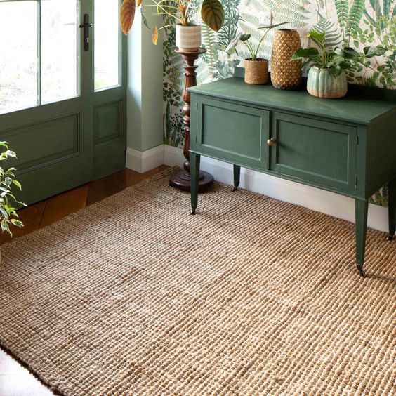 a modern entryway with a botanical wallpaper wall, a green console table with greenery, a jute rug and some other decor