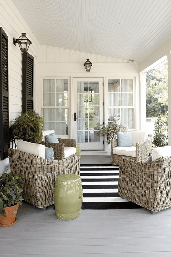 a modern farmhouse porch with elegant wicker chairs and pillows, potted greenery and blooms, a side table and cool lanterns