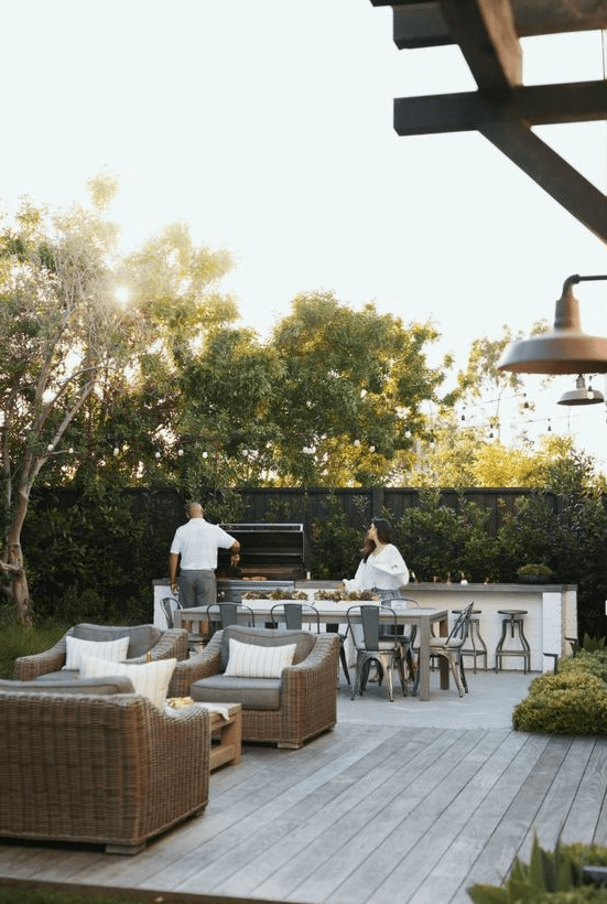a modern farmhouse terrace done in neutrals, with wicker seating furniture, a wooden table, a table and metal chairs, a bar counter with a grill