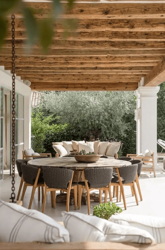 a modern farmhouse terrace with a round table, wicker chairs, a sofa and chairs and some greenery is a lovely space