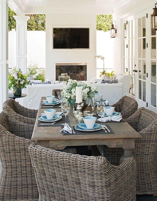 a modern farmhouse terrace with a stained table and wicker chairs, a fireplace and white seatign furniture