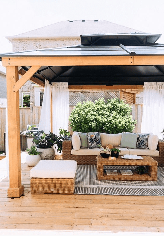 a modern farmhouse terrace with a striped rug, wicker seating furniture, a wicker coffee table, potted plants and printed pillows