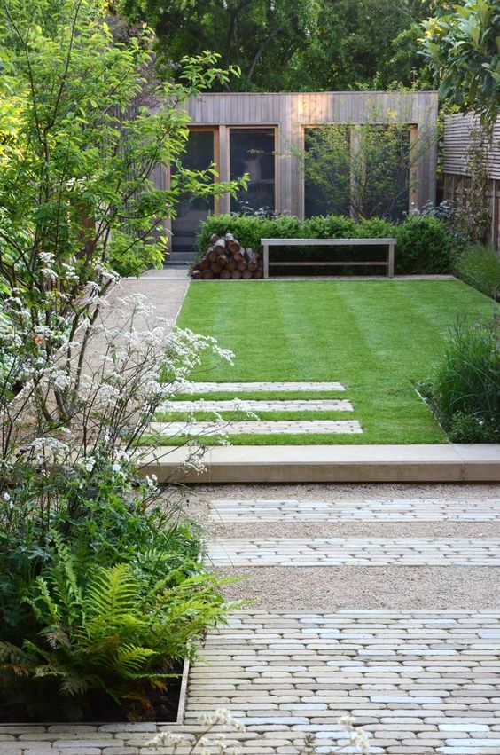 a modern garden with a green lawn, a bench, some greenery and blooms and some shrubs is cool
