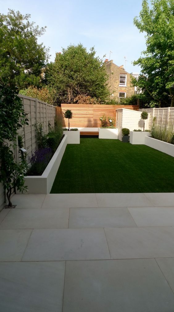 a modern garden with a green lawn, a raised garden bed with greenery and grasses, a built-in bench and a deck done with pavements