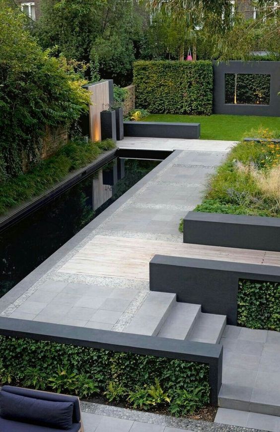a modern garden with a green lawn, a water body, some grasses and greenery plus trees is gorgeous