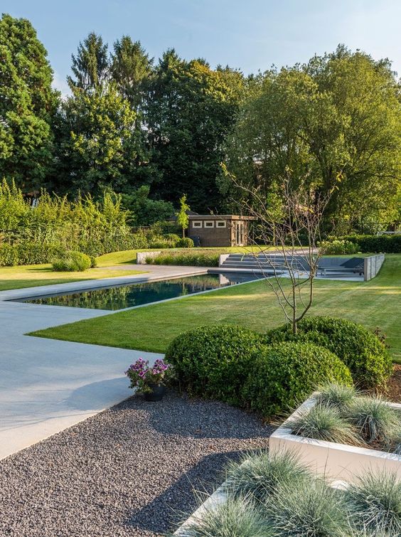 a modern garden with a green lawn, a water body, some shrubs and trees is a chic space that looks very appealing