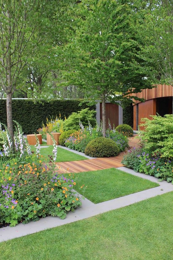 a modern garden with a green lawn, bright blooms and greenery, a wooden garden path, wooden stools