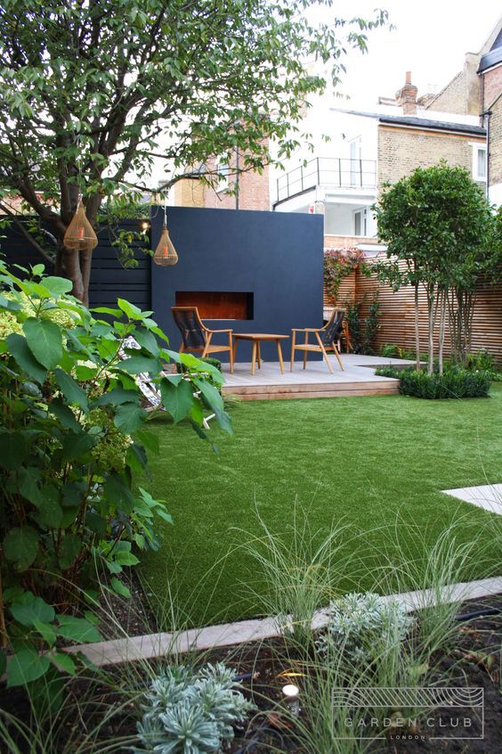 a modern garden with a green lawn, some shrubs and trees, a deck with chairs and a table, pendant lamps is amazing