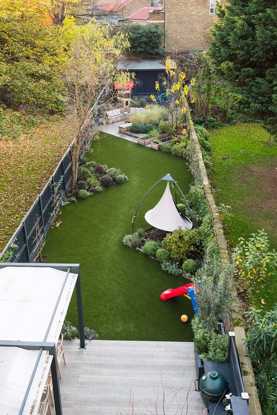 a modern garden with a green lawn, some shrubs and trees, a swing and some garden furniture